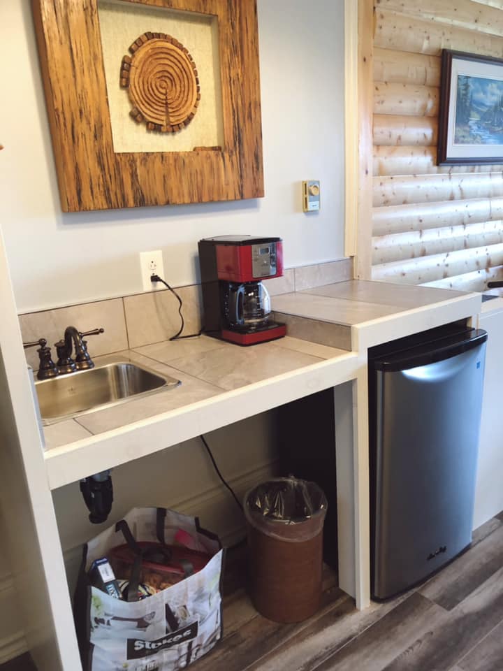 A photo of the kitchenette with mini fridge, counter with coffee pot, and sink with roll up access underneath.