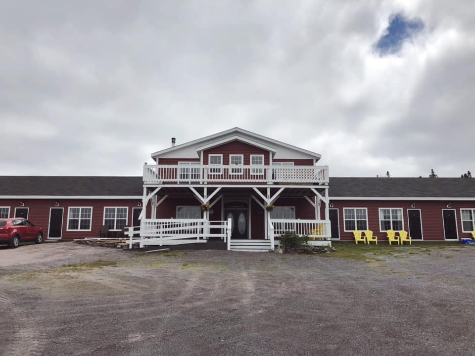 A photo of the exterior of Round Da Bay inn, a large two story red inn with white trim and decks, with two wings of single story rooms on either side of the middle two story building.