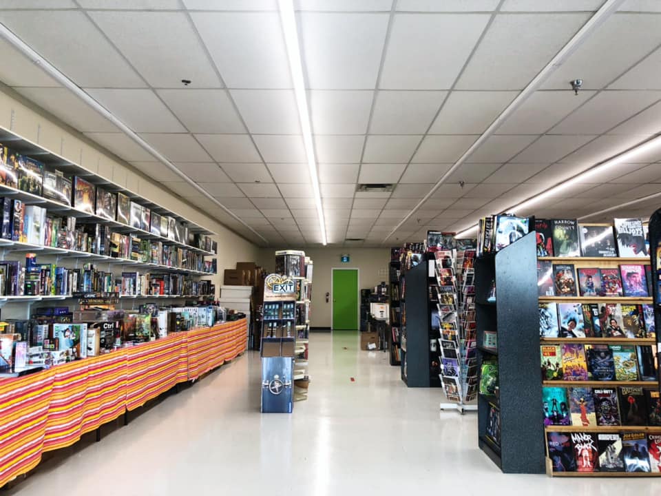 A photo of the back aisle of TimeMasters with board games against the wall on the left and aisles with shelves of comics to the right.