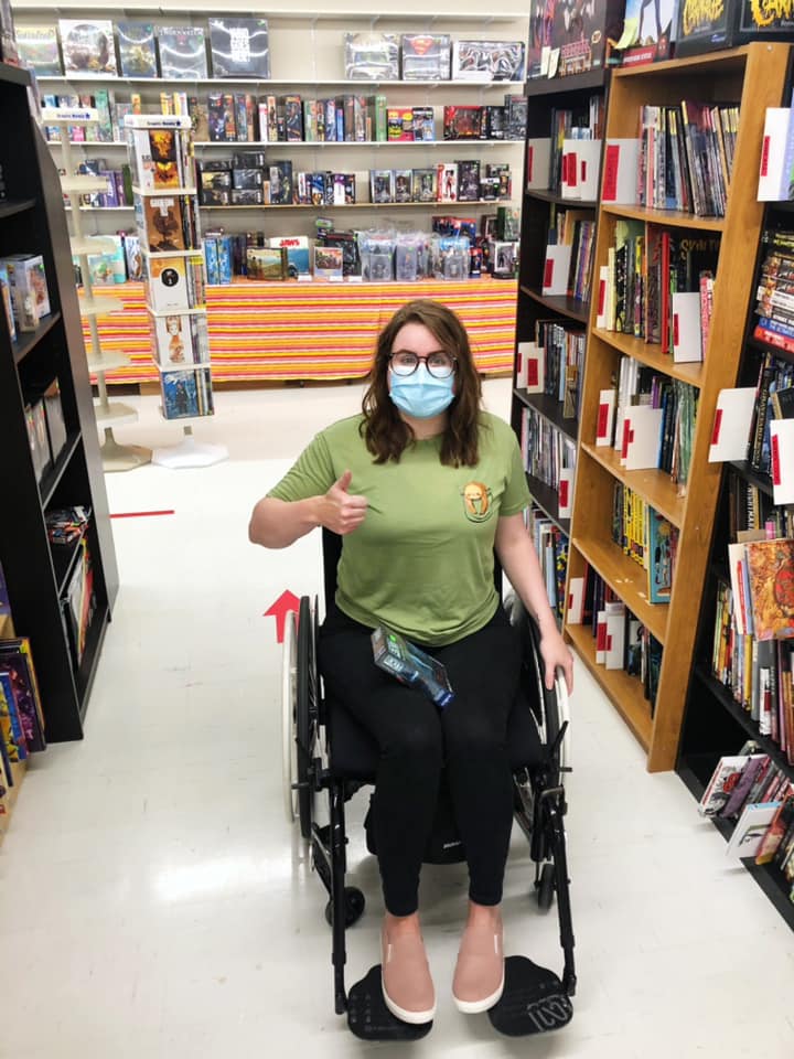  A photo of Lisa sitting in her wheelchair giving a thumbs up in an aisle of comic books.