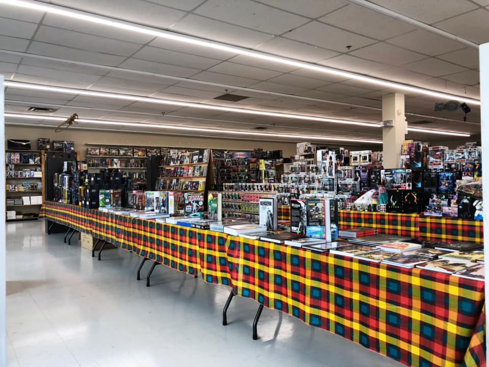 A photo taken from one corner of TimeMasters that shows several long tables filled with books and merchandise and in the background are shelves of more merchandise.