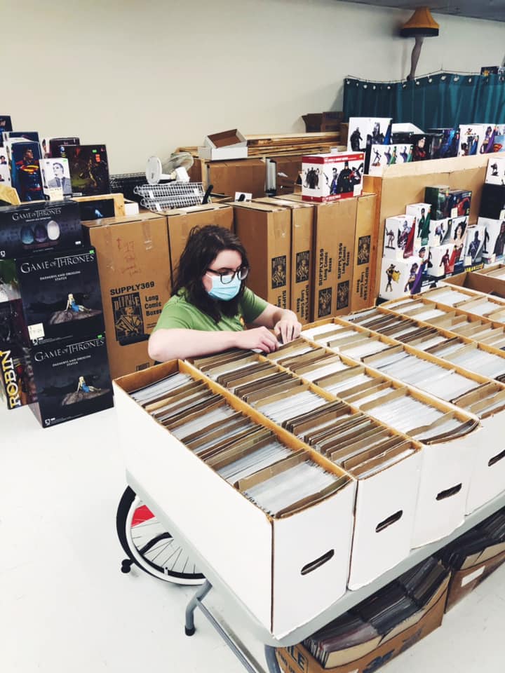 A photo of me sitting in my wheelchair looking through a box of comics on a table.