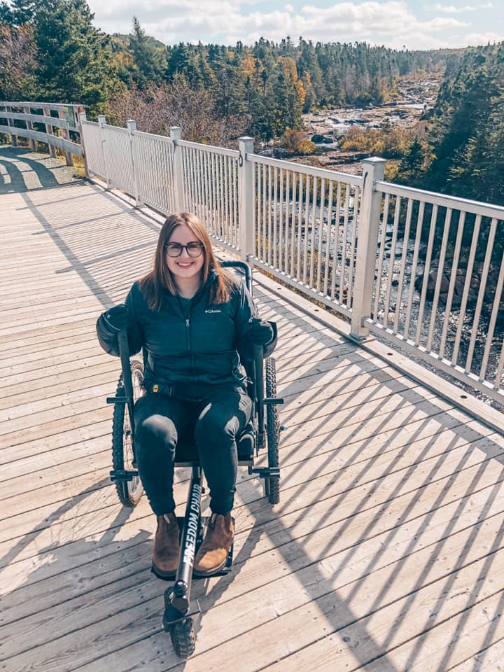 Me sitting in the Grit Freedom Chair on a bridge overlooking Manuels River. 