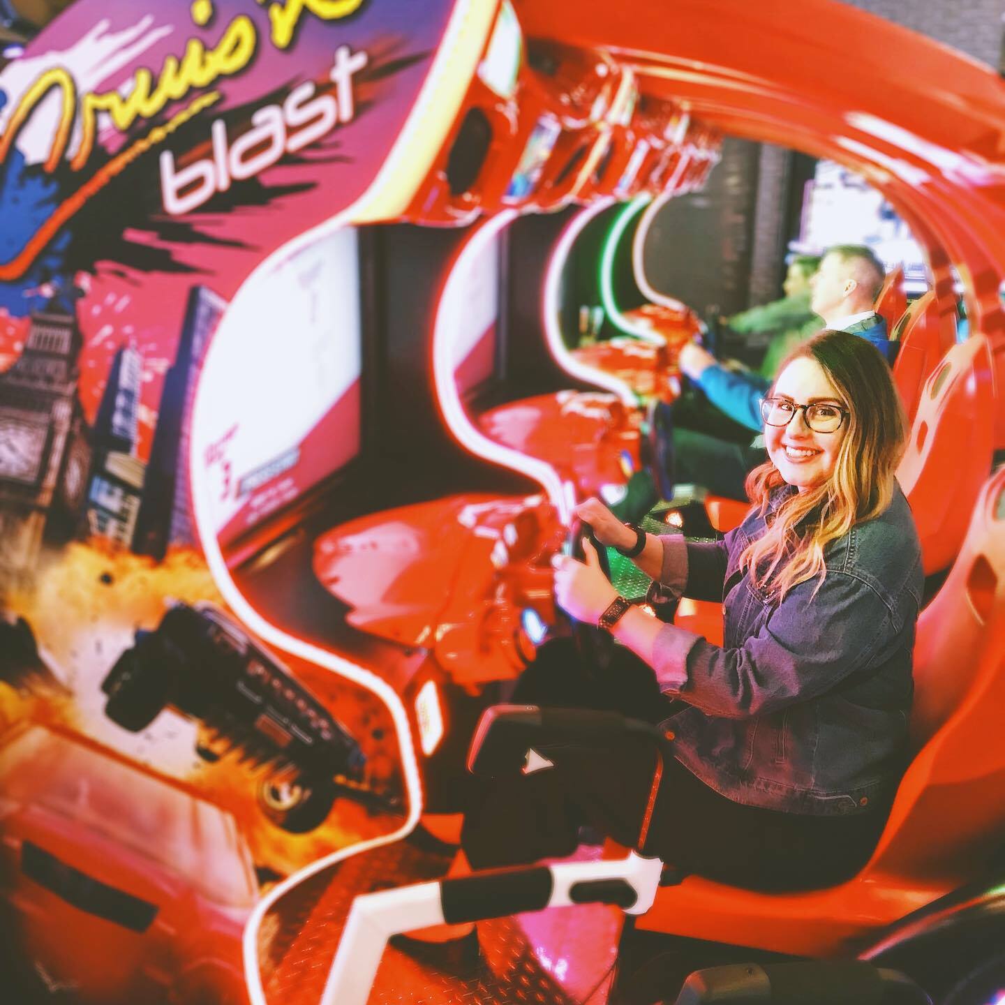 Lisa sitting behind the steering wheel at a racing arcade game.