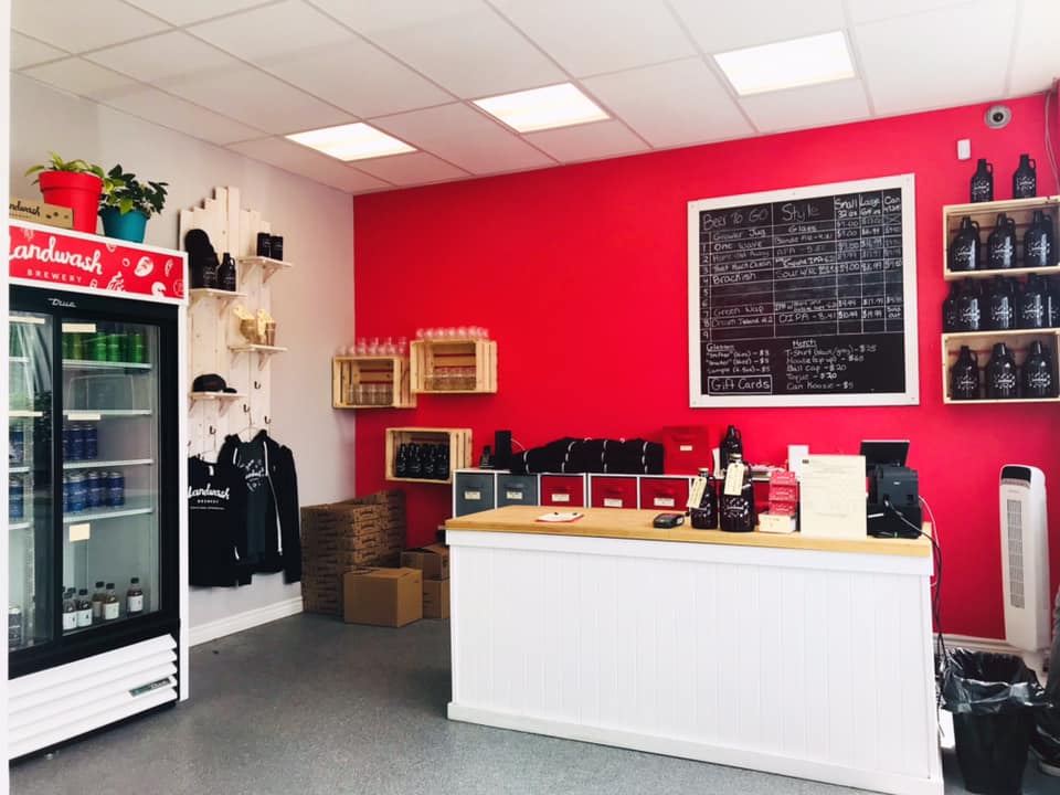 The shop area of the brewery. There’s a red focal wall with a counter and merchandise displayed all around.
