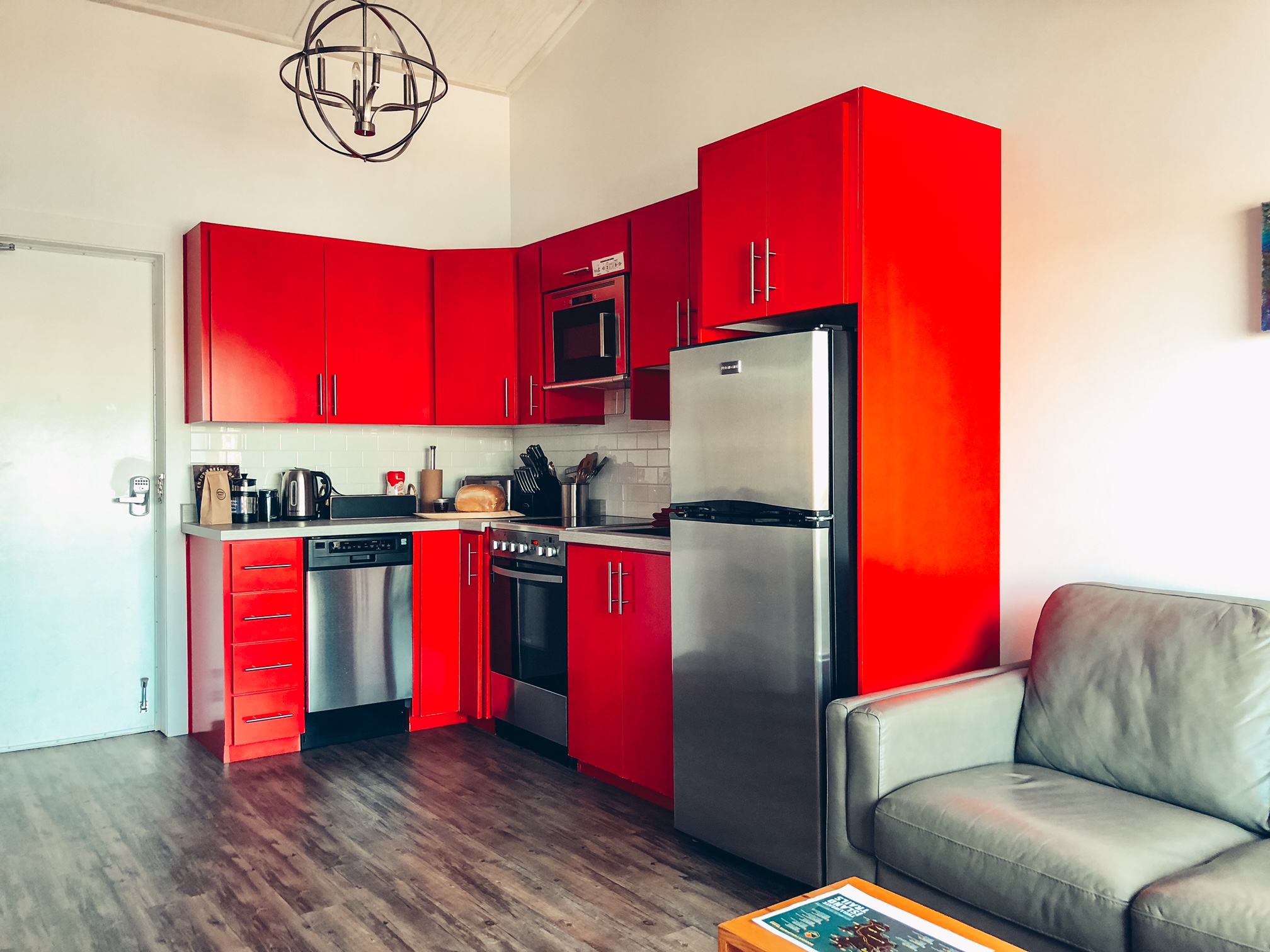 A photo of the self-catering kitchen in the suite, next to the living room area. The shelves are all bright red and the appliances are stainless steel.
