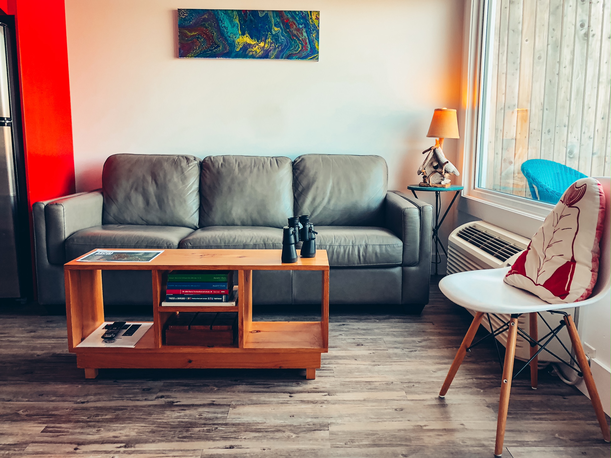 A photo of the living room area of the suite. There is a large window on the right with a white chair near it, as well as a grey leather couch against the back wall with a coffee table in front of it.