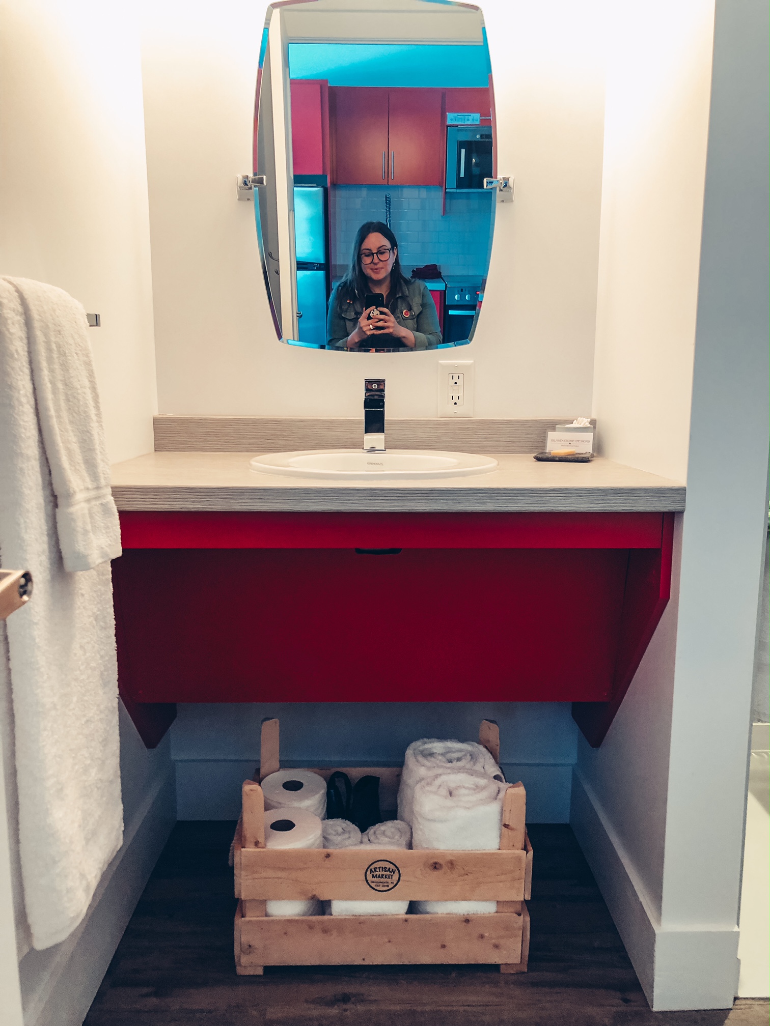 A photo of the bathroom sink and counter. There is a red counter with space to roll under it. Beneath that space is a box of toiletries that can be moved if you need access. Above the sink is a mirror which tilts up and down.