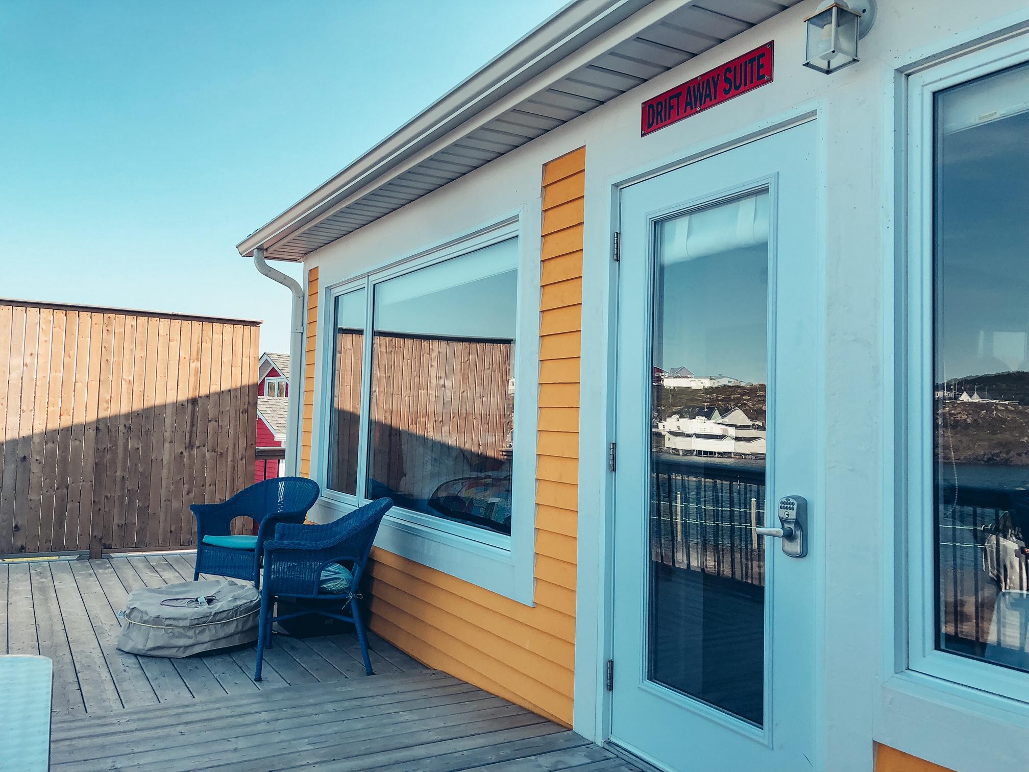 A photo of one part of the deck of the suite, showing some large windows, a wide door, 2 patio chairs and a covered fire pit.