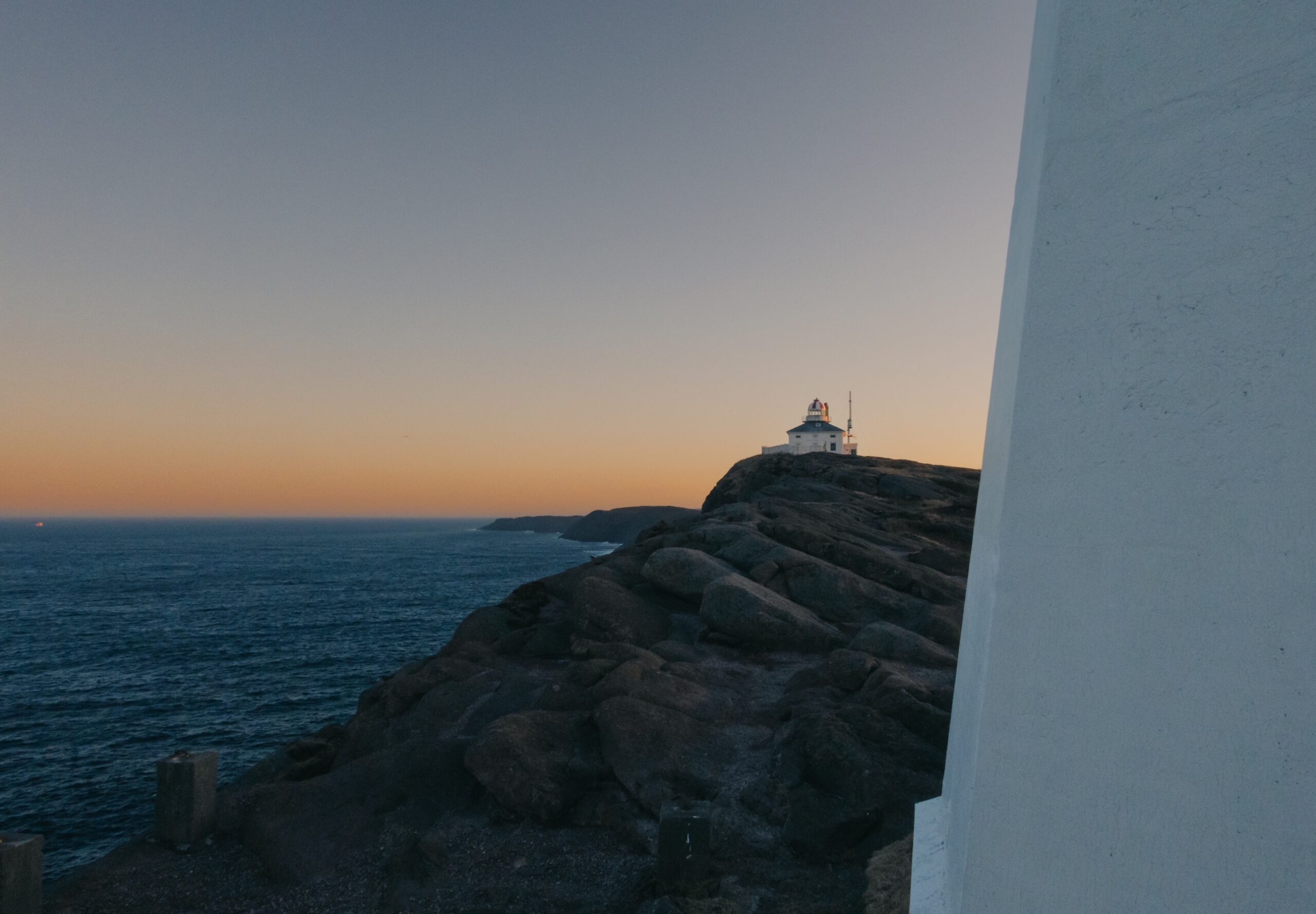 A photo of a lighthouse on the rocks by the ocean taken at sunset. 