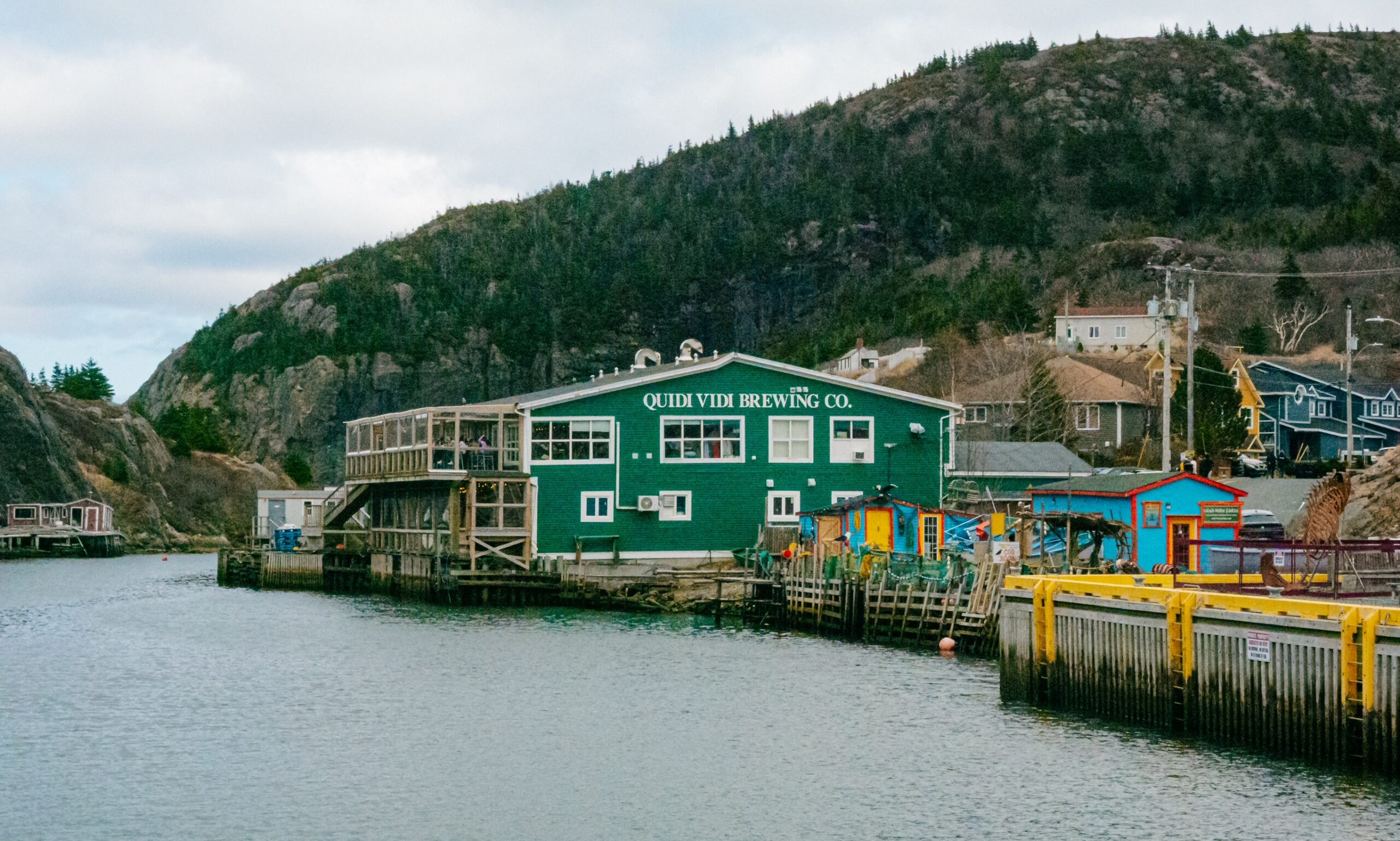 A view of the harbour in Quidi Vidi, with some fishing stages on the sides and a large green building - Quidi Vidi Brewery in the background. 