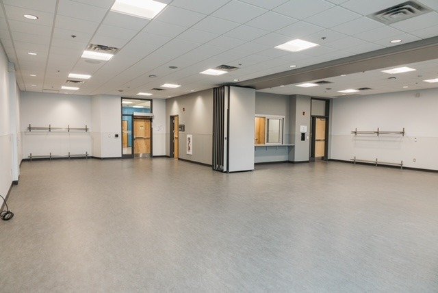A large multi-purpose room that can be partitioned into two smaller rooms. Along the back wall you can see into the kitchen area. 