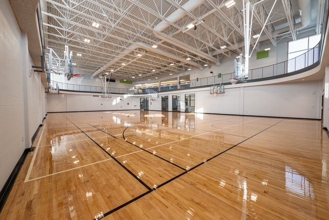 A full size gymnasium with shiny hardwood floors and basketball nets.