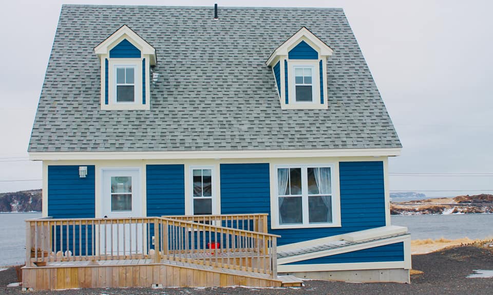 Image: A photo of the exterior of Blueberry Cottage - a dark blue house A frame house with white trim. Photo credit: Artisan Inn.