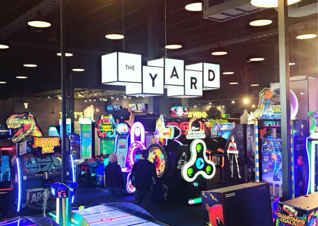 a picture of the arcade area of The Rec Room with a large sign overheard that reads: The Yard.